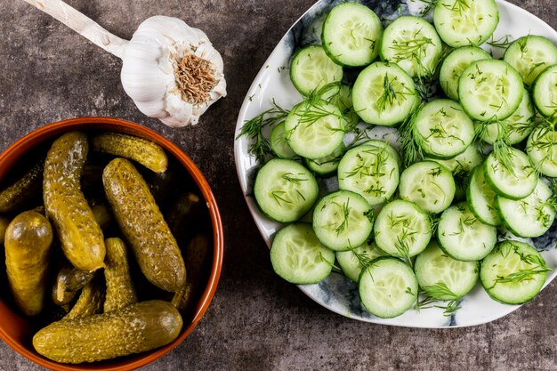 Cetriolo di vista superiore affettato fresco con aneto sul piatto e marinato in ciotola sulla pietra marrone