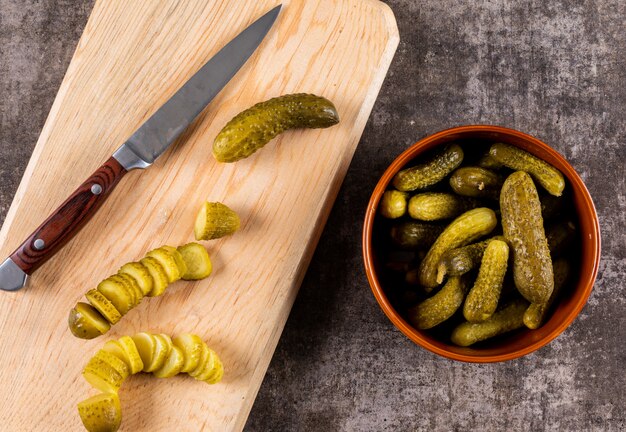 Cetriolo marinato vista dall'alto affettato sul tagliere di legno e nella ciotola sulla pietra marrone