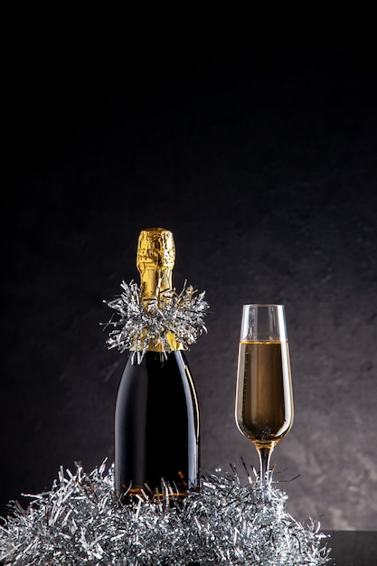 Champagne vista frontale in bottiglia e bicchiere su superficie scura