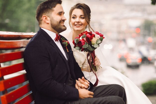 Charme sposa e sposo si tengono teneri seduti sulla panchina fuori