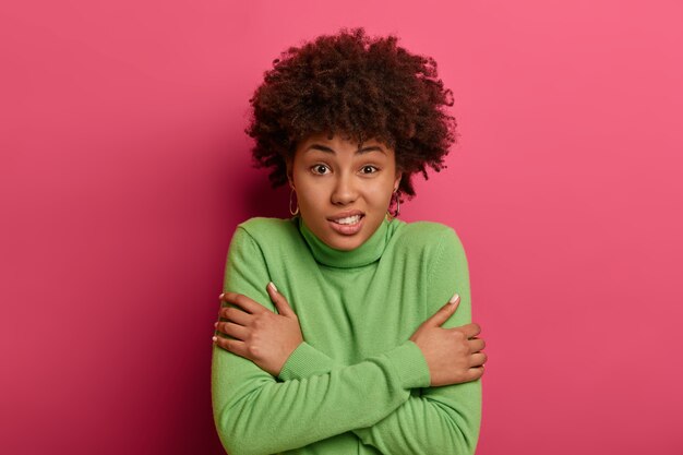 Che freddo. La signora dalla pelle scura perplessa si abbraccia, trema per il freddo, cammina con il vento, scuote e stringe i denti, vestita con un maglione verde