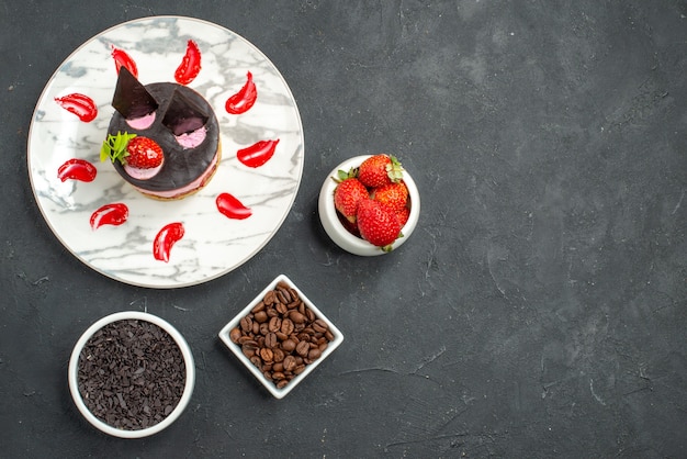 Cheesecake alla fragola vista dall'alto su ciotole di piatto ovale bianco con fragole e semi di caffè al cioccolato su sfondo scuro