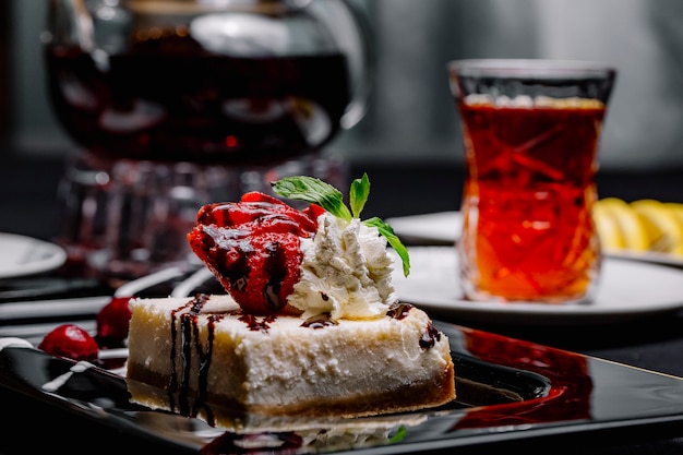 Cheesecake di vista laterale con sciroppo di cioccolato fragola menta panna montata ciliegia e tè nero