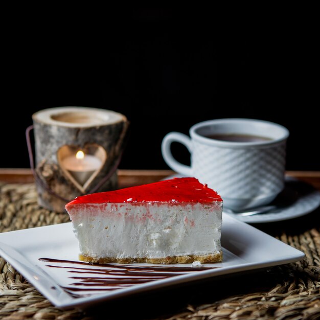 Cheesecake di vista laterale con una tazza di tè e candela nel servire tovaglioli