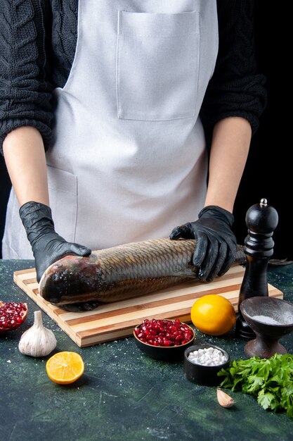 Chef di vista frontale con guanti neri che mette pesce crudo sul tagliere macinapepe semi di melograno in una ciotola sul tavolo