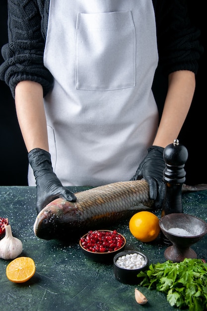 Chef di vista frontale in grembiule che mette pesce crudo sul tagliere macinapepe semi di melograno in una ciotola sul tavolo