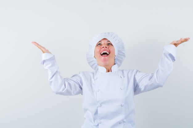 chef donna alzando palme sparse in uniforme bianca e guardando felice.