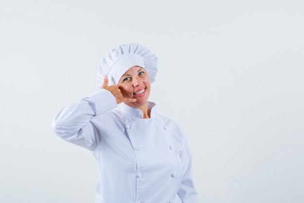 chef donna che mostra il gesto della telefonata in uniforme bianca e sembra ottimista.