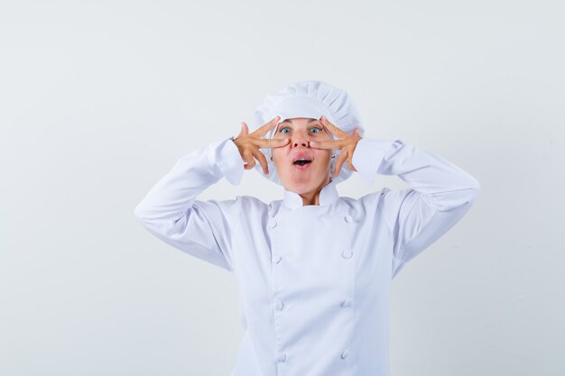chef donna in uniforme bianca che mostra il gesto di vittoria sugli occhi e guardando stupito
