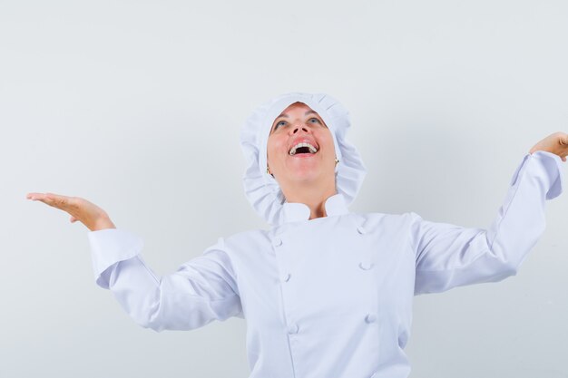 chef donna in uniforme bianca diffondendo palme da parte mentre guarda in alto e sembra felice