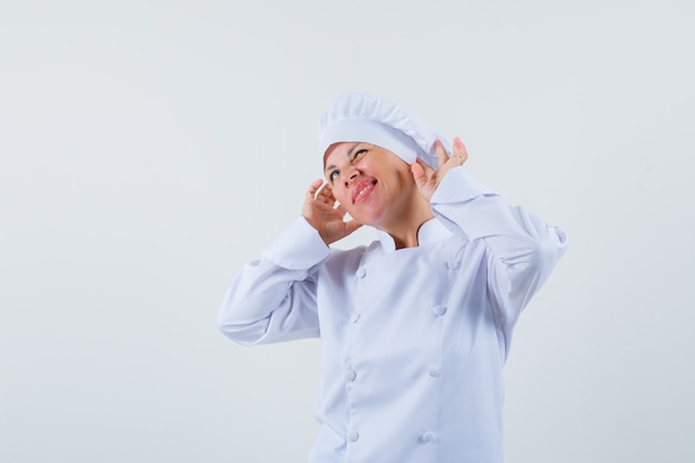 chef donna in uniforme bianca in posa come indossare gli auricolari e guardando divertito