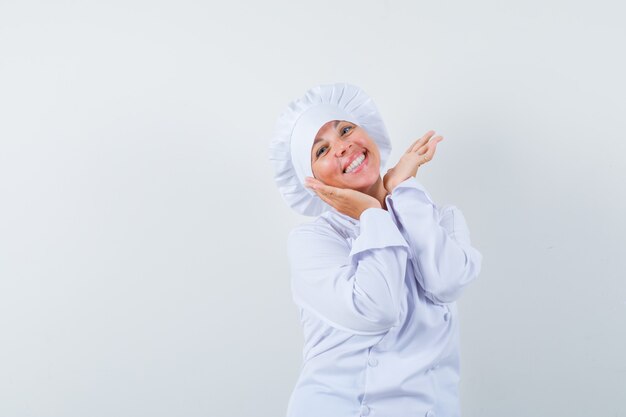 chef donna mano nella mano sotto il mento in uniforme bianca e dall'aspetto carino