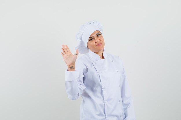 Chef femminile in uniforme bianca agitando la mano per il saluto e guardando fiducioso