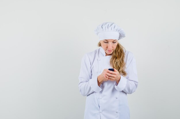 Chef femminile in uniforme bianca utilizzando il cellulare e guardando occupato