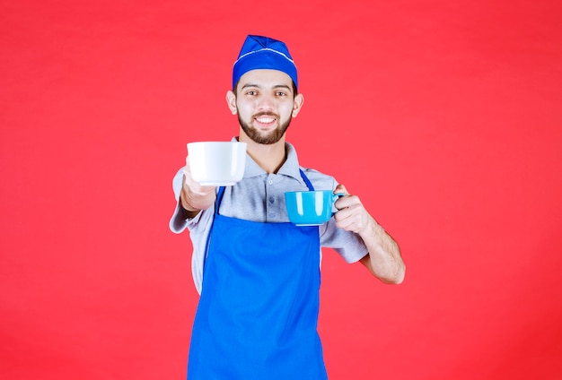 Chef in grembiule blu che tiene in entrambe le mani tazze di ceramica blu e bianche e serve al cliente.