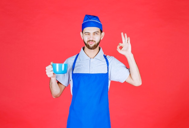 Chef in grembiule blu che tiene in mano una tazza di ceramica blu e si gode il gusto del prodotto.