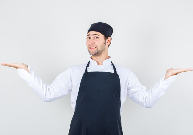 Chef maschio che alza le braccia spalancate come prendere qualcosa in uniforme, grembiule e sembrare allegro. vista frontale.