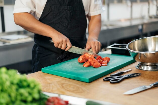 Chef maschio con grembiule per affettare i pomodori in cucina