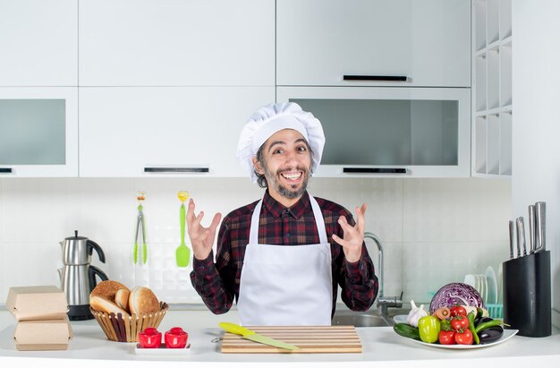 Chef maschio eccitato vista frontale in piedi dietro il tavolo della cucina in cucina