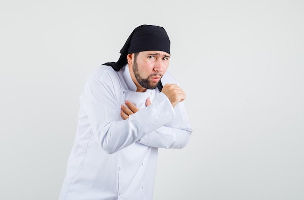 Chef maschio in uniforme bianca che soffre di mal di gola e tosse e sembra malato, vista frontale.