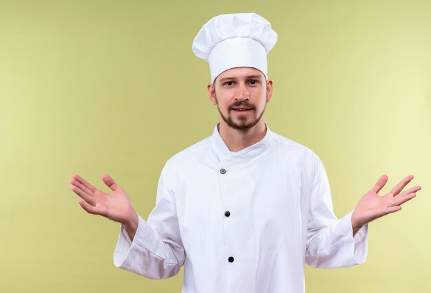 Chef maschio professionista cuoco in uniforme bianca e cappello da cuoco diffondendo le mani sorridente in piedi amichevole su sfondo verde