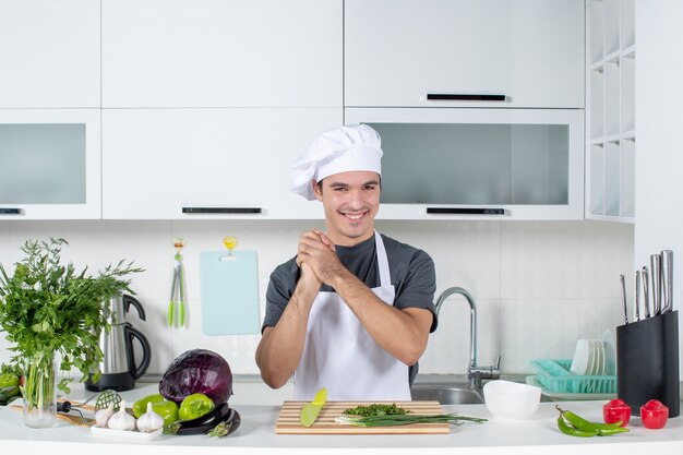 Chef maschio vista frontale in uniforme con le mani giunte dietro il tavolo della cucina