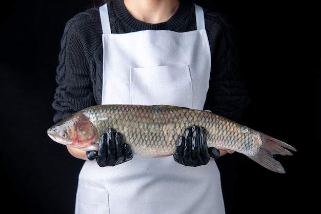 Chef vista frontale con guanti neri che tengono pesce fresco su superficie scura