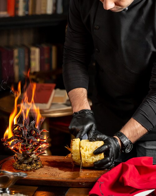 Cheff tagliando l'ananas a fette accanto alla cima frondosa che brucia