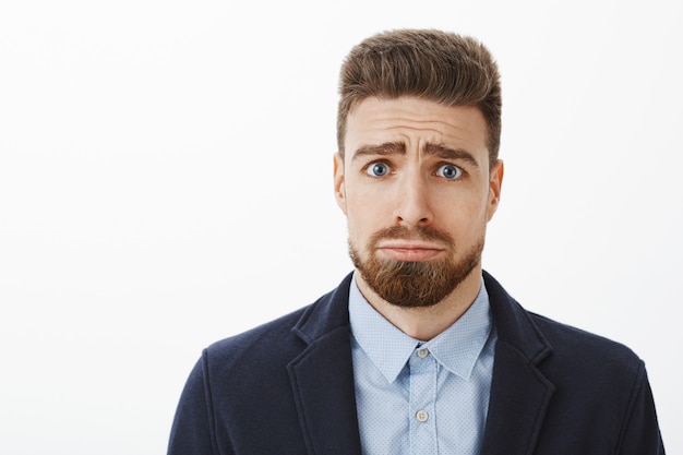 Chi può rifiutare questo cutie con gli occhi azzurri. Affascinante ragazzo bello e carismatico con la barba e le sopracciglia malate aggrottando le sopracciglia facendo il viso sciocco e carino imbronciato chiedendo favore o scusandosi