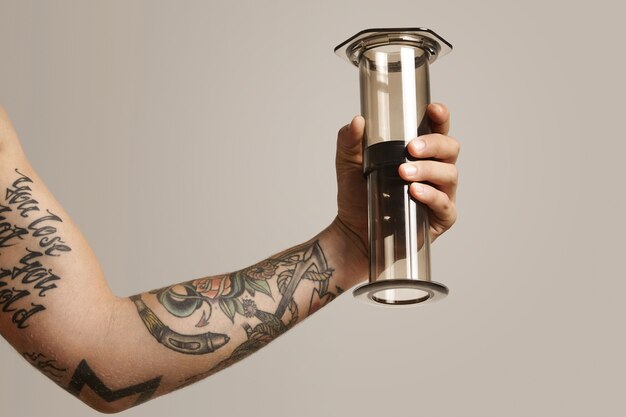 Chiara aeropress grigio chiaro con riflessi tenuti da un giovane tatuato, ritratto da vicino