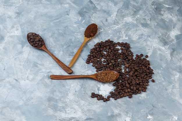 Chicchi di caffè con caffè istantaneo, farina di caffè, chicchi di caffè in primo piano cucchiai di legno su uno sfondo di marmo azzurro