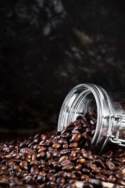 Chicchi di caffè in un barattolo di vetro su sfondo nero closeup messa a fuoco selettiva cornice verticale Torrefazione e preparazione del caffè cornice verticale