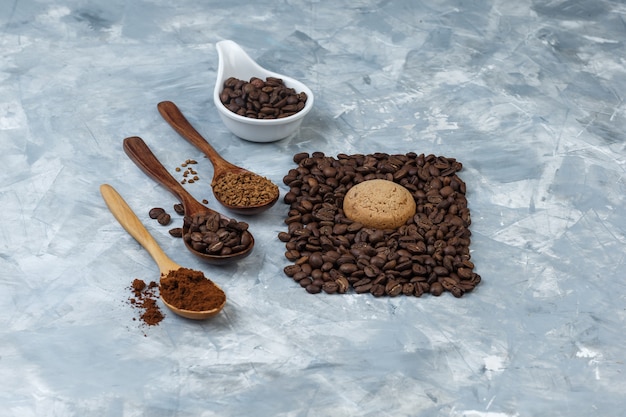 Chicchi di caffè in una brocca di porcellana bianca con chicchi di caffè, caffè istantaneo, farina di caffè in cucchiai di legno ad alto angolo di visione su uno sfondo di marmo azzurro