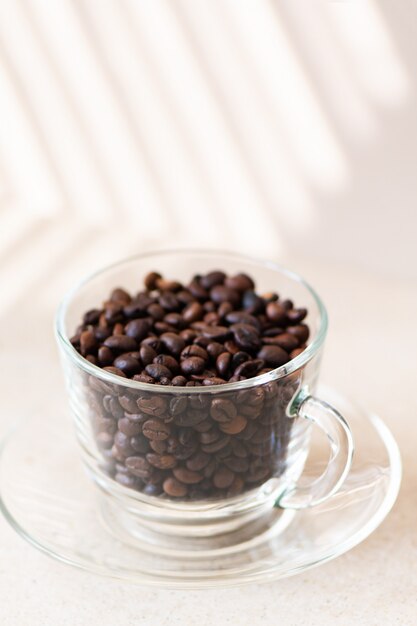 Chicchi di caffè in una tazza di vetro su una tabella.