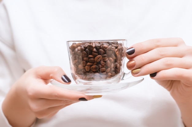 Chicchi di caffè in una tazza di vetro sulle mani femminili.