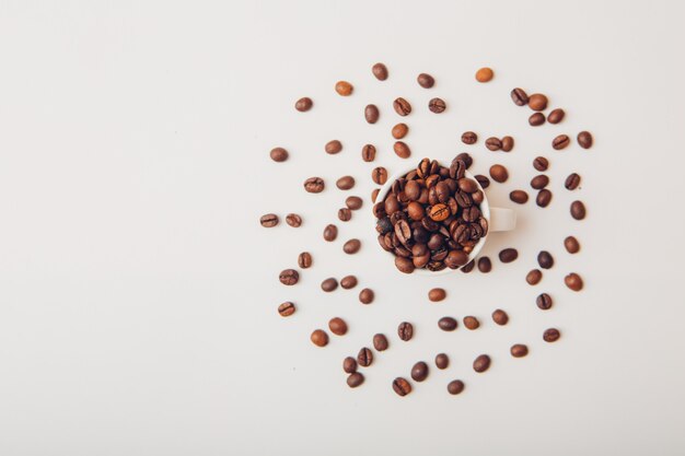 Chicchi di caffè in una vista superiore della tazza su una tavola bianca