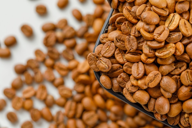 Chicchi di caffè marrone in un cestino nero su fagioli sparsi. Veduta dall'alto.