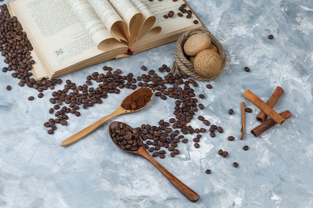Chicchi di caffè piatti laici, caffè istantaneo in cucchiai di legno con libro, cannella, biscotti, corde su sfondo di marmo blu scuro e chiaro. orizzontale