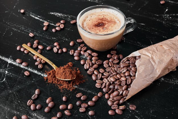 Chicchi di caffè su sfondo nero con una tazza di bevanda.