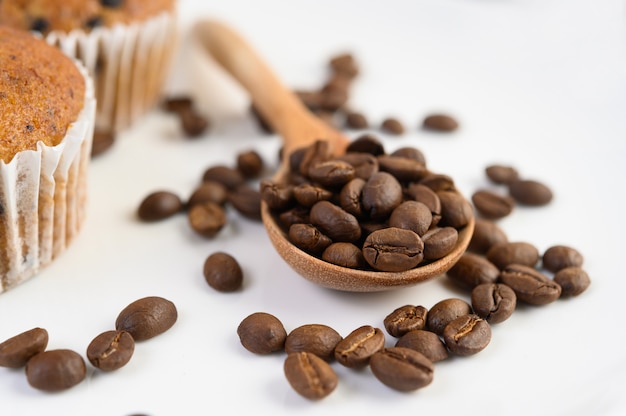 Chicchi di caffè sul cucchiaio di legno e cupcakes alla banana su un tavolo di legno bianco.