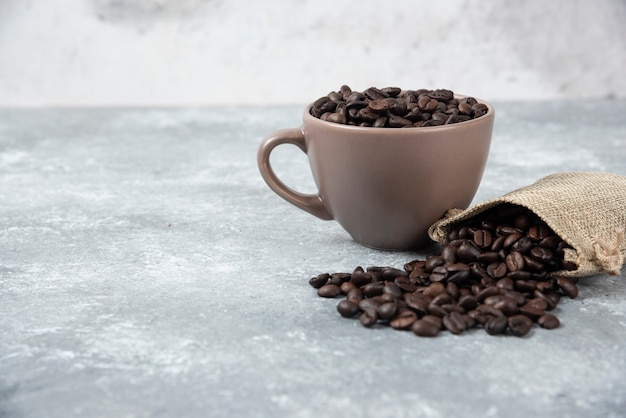 Chicchi di caffè tostati dal sacco di iuta e in tazza su marmo.