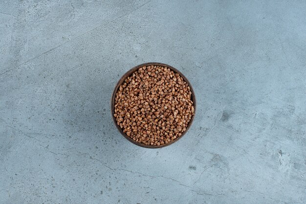 Chicchi di grano saraceno in una tazza di legno su sfondo blu. Foto di alta qualità