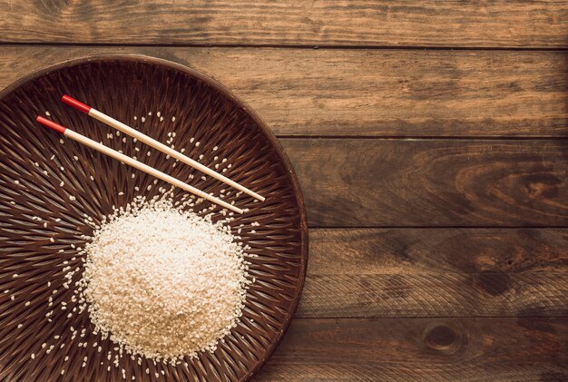 Chicchi di riso bianco con le bacchette sul piatto di legno sopra il tavolo