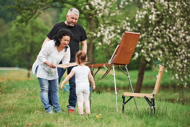 Chiedere una prova. Nonna e nonno si divertono all'aperto con la nipote. Concezione della pittura