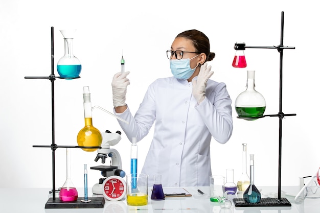 Chimico femminile di vista frontale in vestito medico con l'iniezione della tenuta della maschera su spruzzata di covid del laboratorio di chimica del virus del fondo bianco