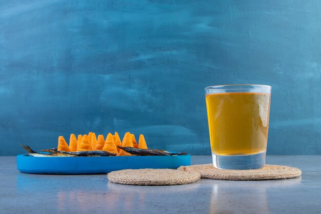 Chip di cono e pesce essiccato su un piatto di legno accanto a un bicchiere di birra su un sottopentola, sullo sfondo di marmo.