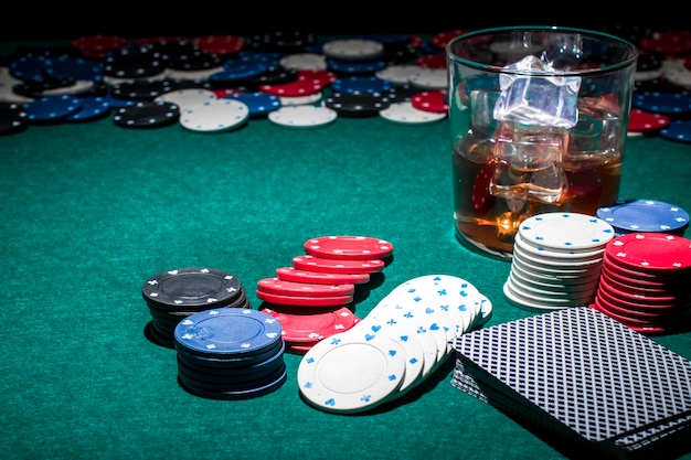 Chip di poker e bicchiere di whisky sul tavolo da poker verde