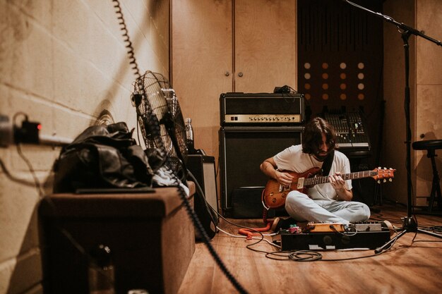 Chitarrista che registra musica rock in studio, seduto sul pavimento