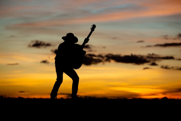 Chitarrista della ragazza della siluetta su un tramonto