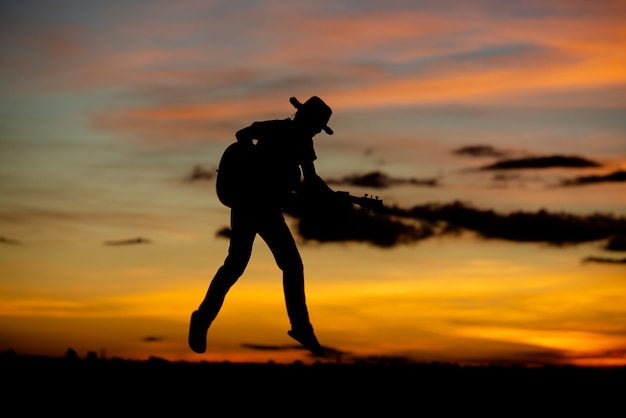 Chitarrista della ragazza della siluetta su un tramonto